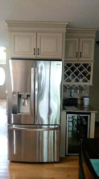 Stainless steel refrigerator in a kitchen with cream cabinets and a built-in wine rack