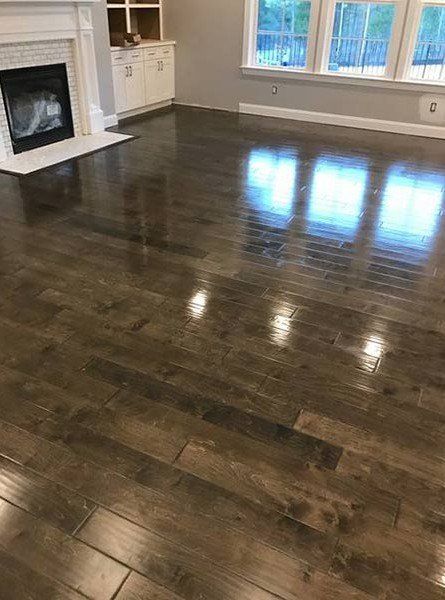 Empty living room with glossy dark hardwood floors, fireplace, and large windows.