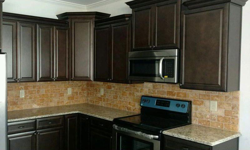 Modern kitchen with dark wood cabinets, tan tile backsplash, black countertops, and stainless steel microwave and stove