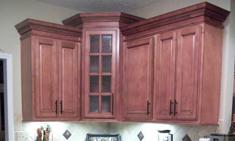 Wooden kitchen cabinets with crown molding and a glass-front center cabinet above a countertop.