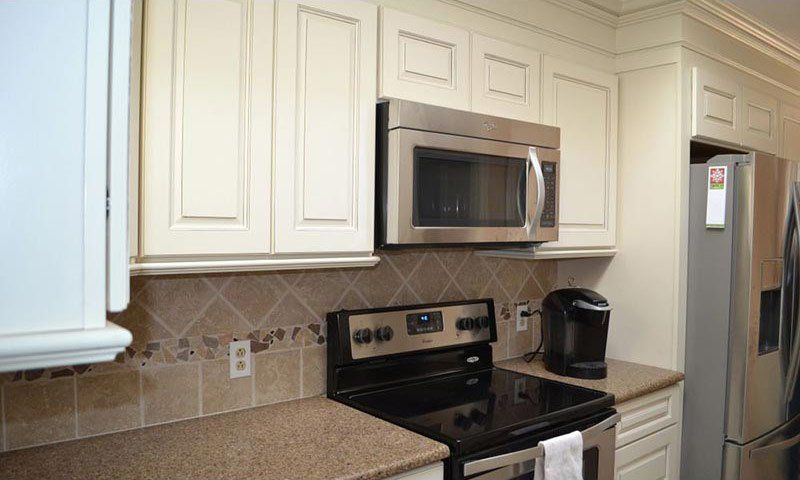 Modern kitchen with white cabinets, stainless microwave, black stove, granite countertop, and stainless fridge