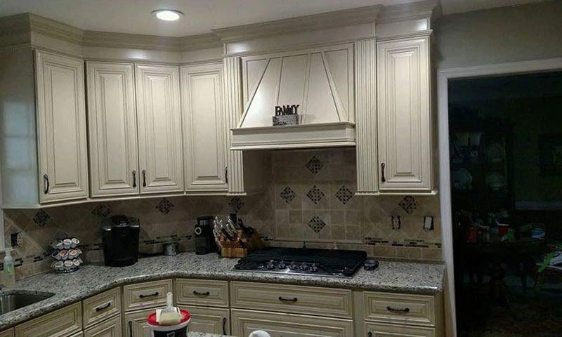 Cream-colored kitchen with cabinets, stove, tiled backsplash, and ceiling lights