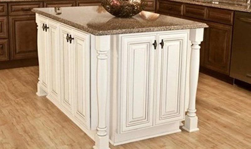 White kitchen island cabinet with ornate trim and dark granite countertop in a wood-floored kitchen