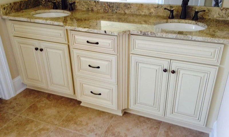 Bathroom vanity with two sinks, cream cabinets, and tan granite countertop
