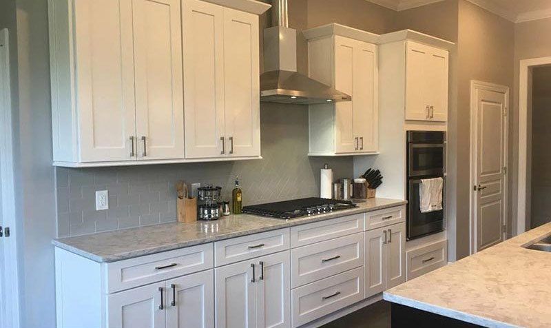 Bright modern kitchen with white cabinets, gray backsplash, gas stove, and stainless steel oven.