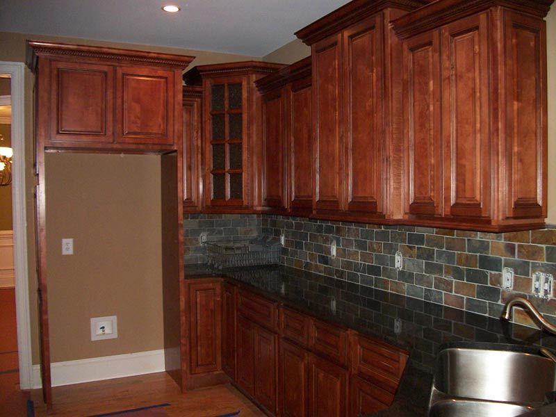 Kitchen with wooden cabinets, dark tile backsplash, and stainless sink on the right.