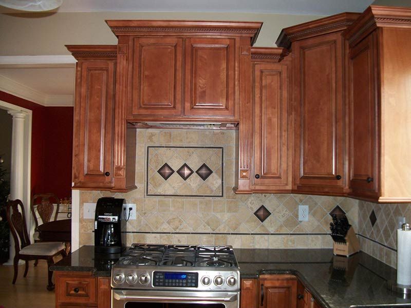 Kitchen with cherry wood cabinets, stainless steel stove, and beige tile backsplash with decorative accents