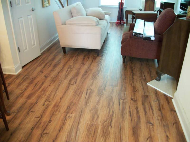 Empty living room with wood-look flooring, white armchair, and maroon sofa near a small table.