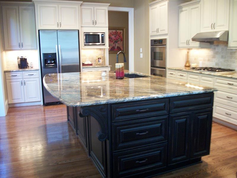Modern kitchen with white cabinets, stainless appliances, and a large granite-topped island with dark base cabinets