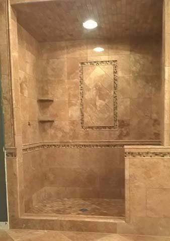 Tiled walk-in shower with recessed shelf, decorative border, and overhead light