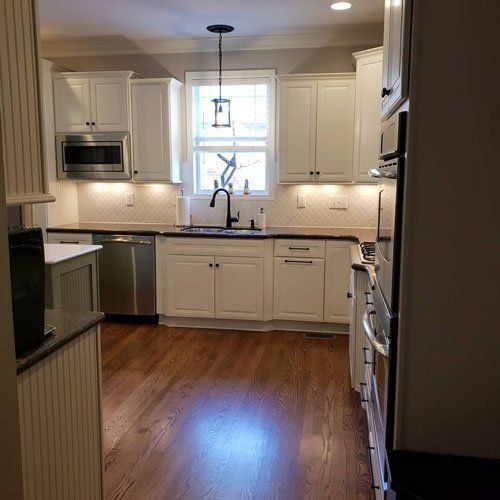 Bright white kitchen with hardwood floor, window over sink, and stainless steel appliances