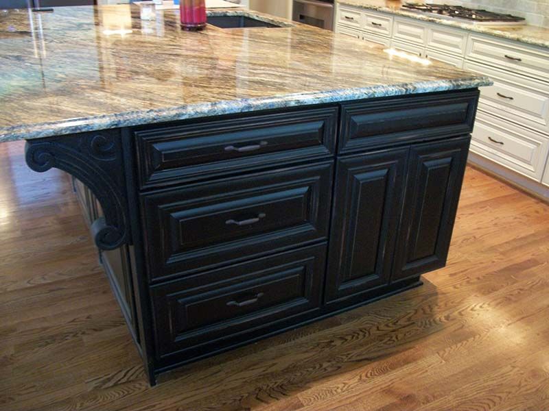 Black kitchen island with granite top on hardwood floor in a showroom kitchen