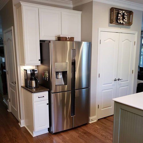 Bright kitchen with stainless steel fridge, white cabinets, and wood floors