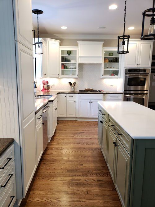 Bright white kitchen with wood floors, teal island, white cabinets, and stainless-steel appliances.