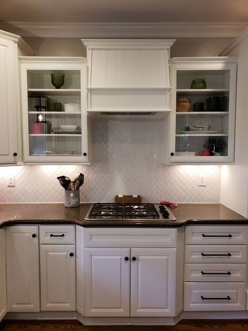 White kitchen with built-in cabinets, gas cooktop, and glass-front shelves above dark countertops.