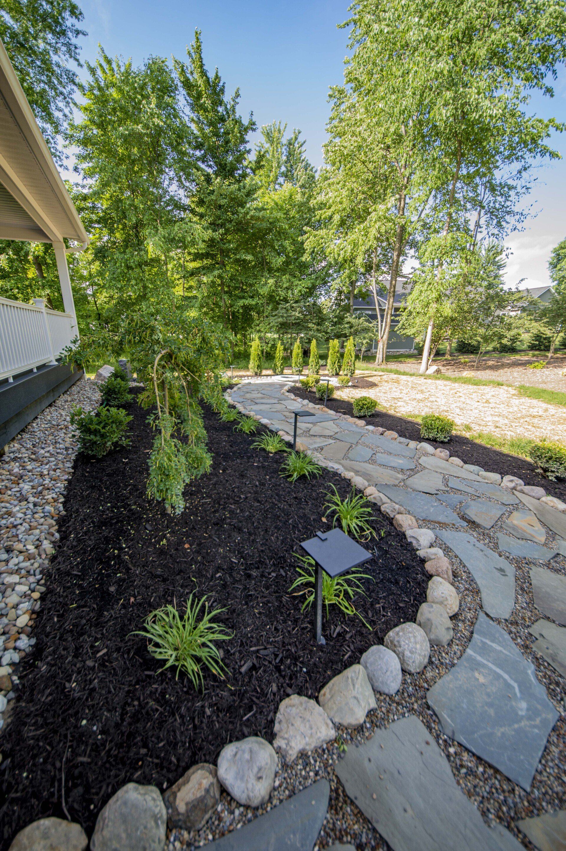 Landscaped garden bed with mulch, stepping stones, and solar lights; trees in background.