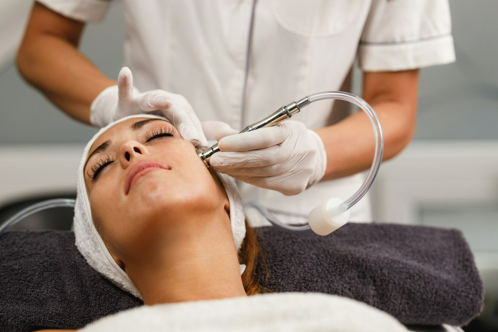 Woman receiving facial treatment in a spa, therapist holding a device over her face.
