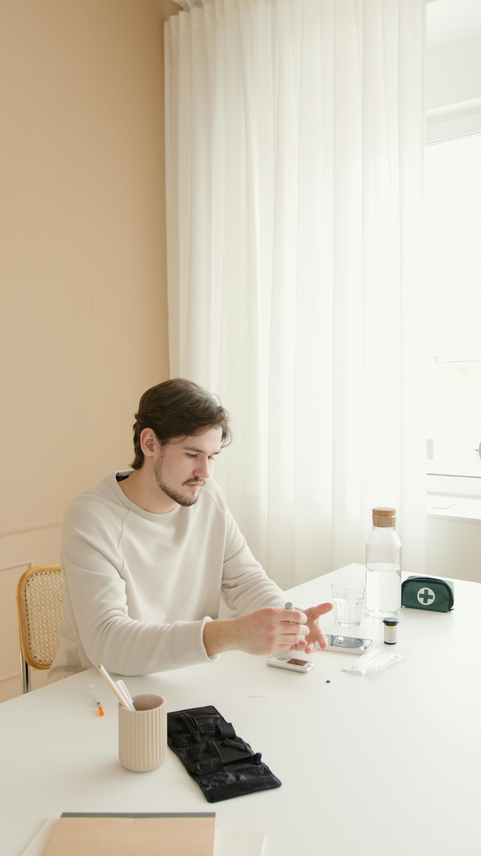Person sitting at a white table, holding a cup in a bright room with sheer curtains.