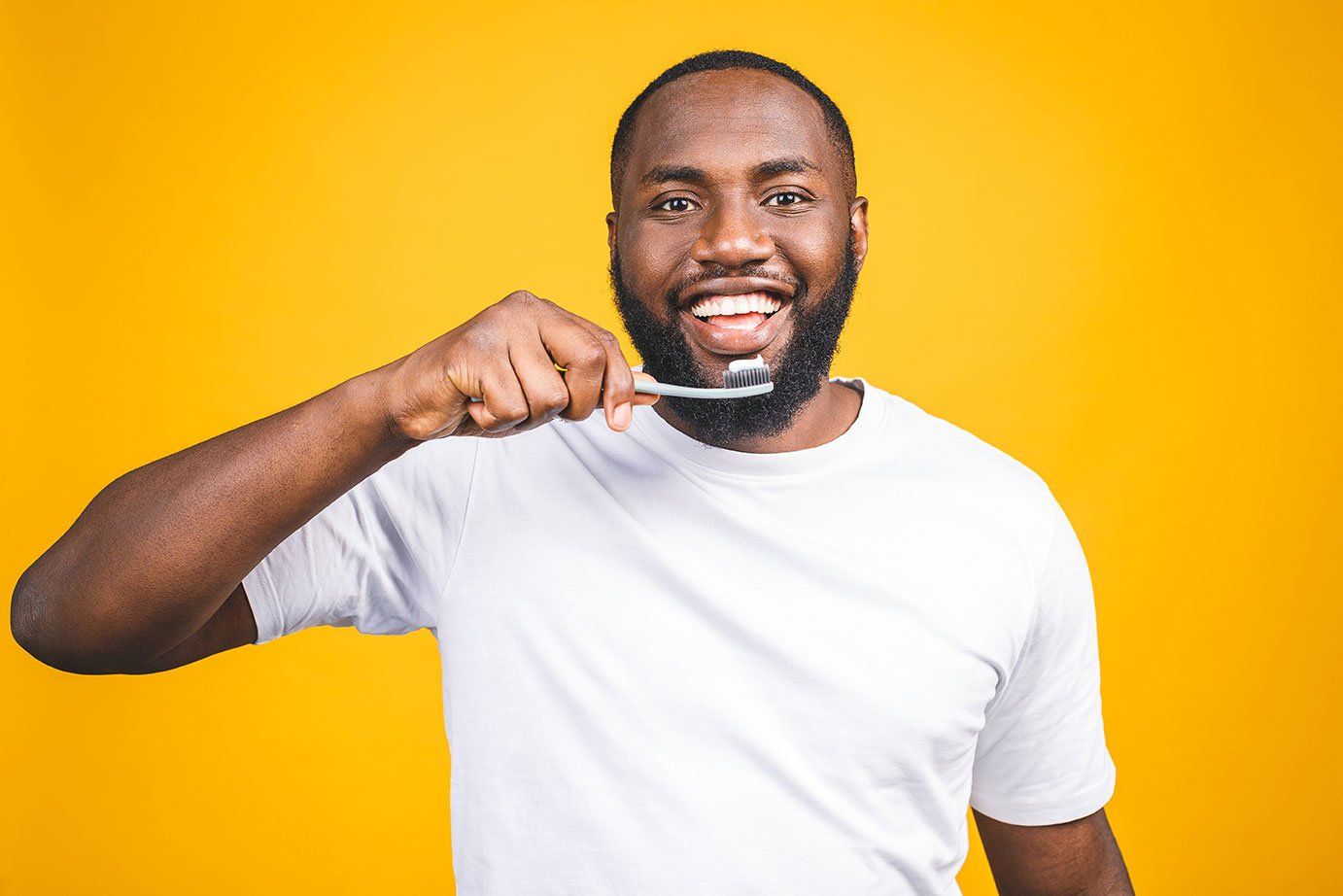 A man is brushing his teeth with a toothbrush and smiling.