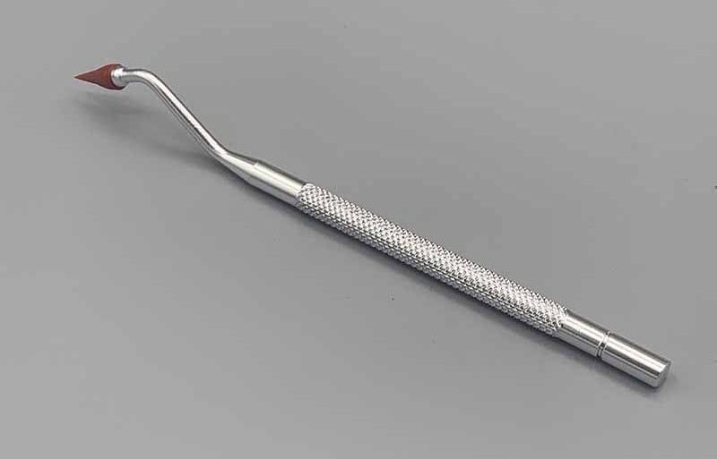 A dental tool with a red tip is sitting on a gray surface.