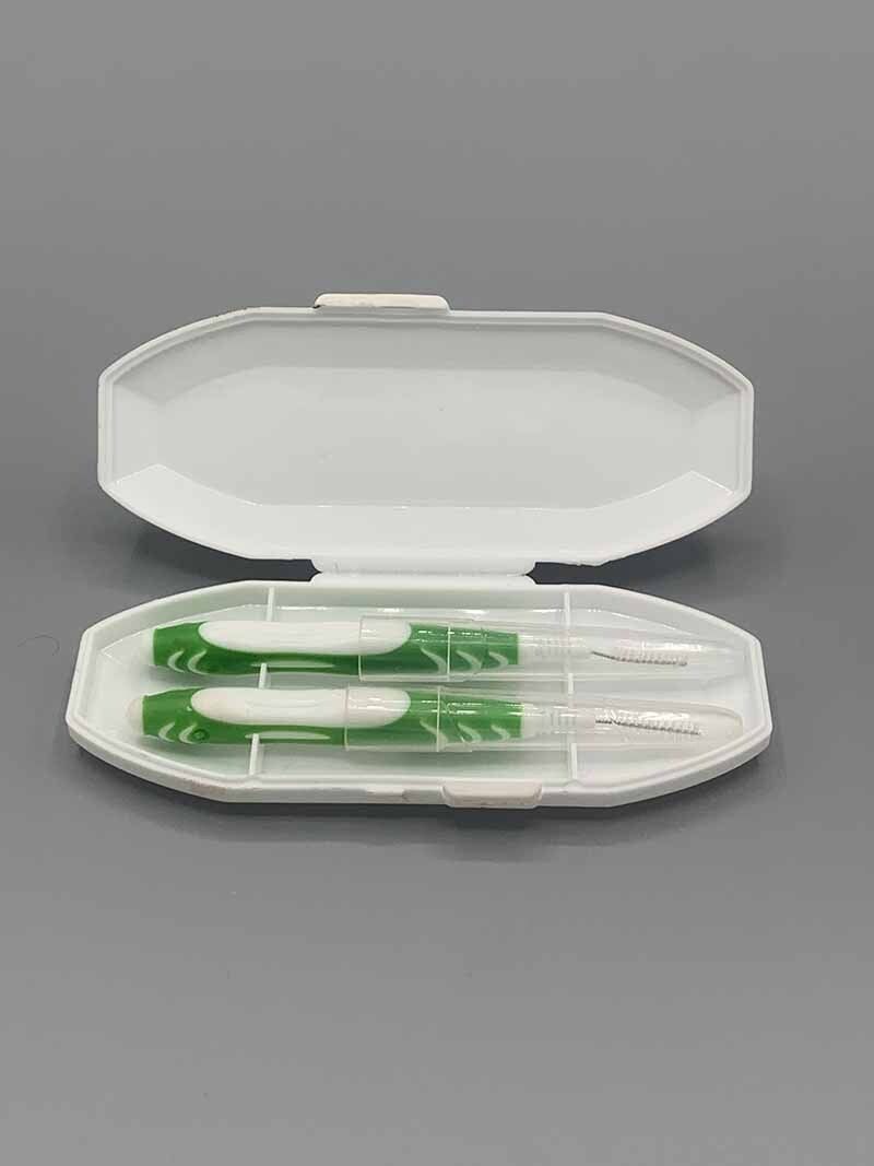 A white plastic case with two green toothpicks inside of it.