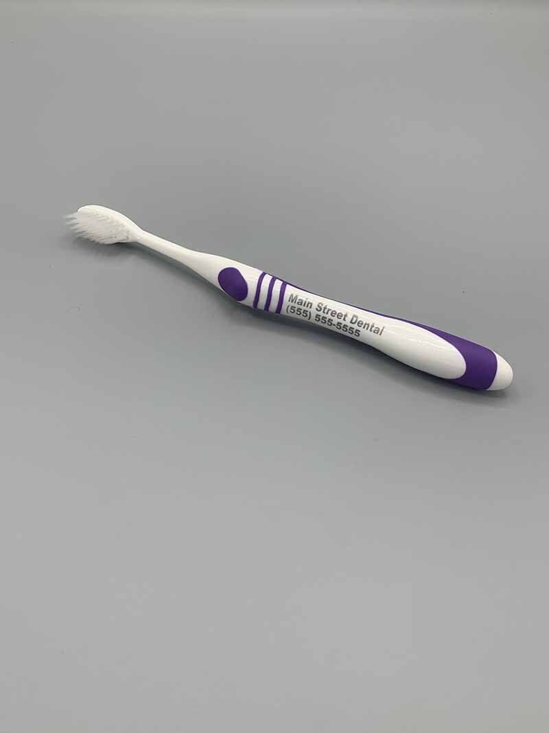 A white and purple toothbrush is sitting on a gray surface.