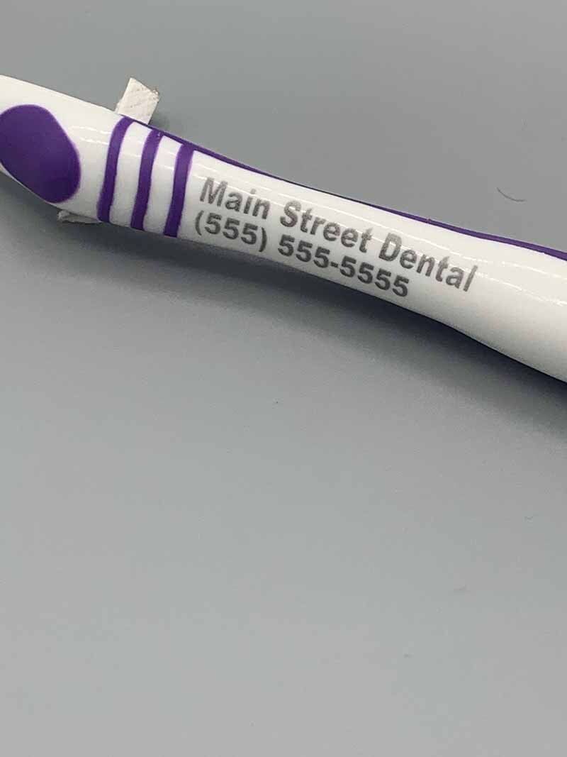 A white and purple pen with the name main street dental on it is sitting on a table.