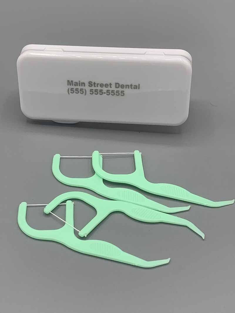 A box of dental floss is sitting on a table next to some floss picks.