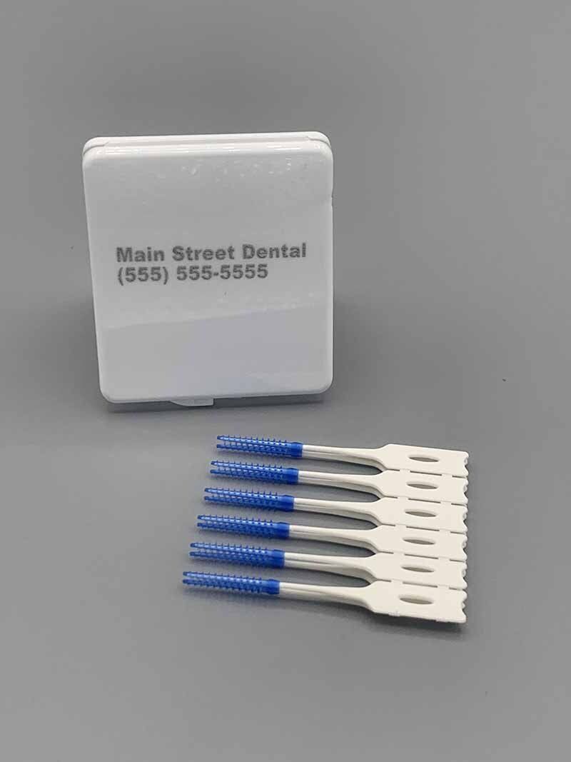 A box of interdental brushes with blue handles is sitting on a table.