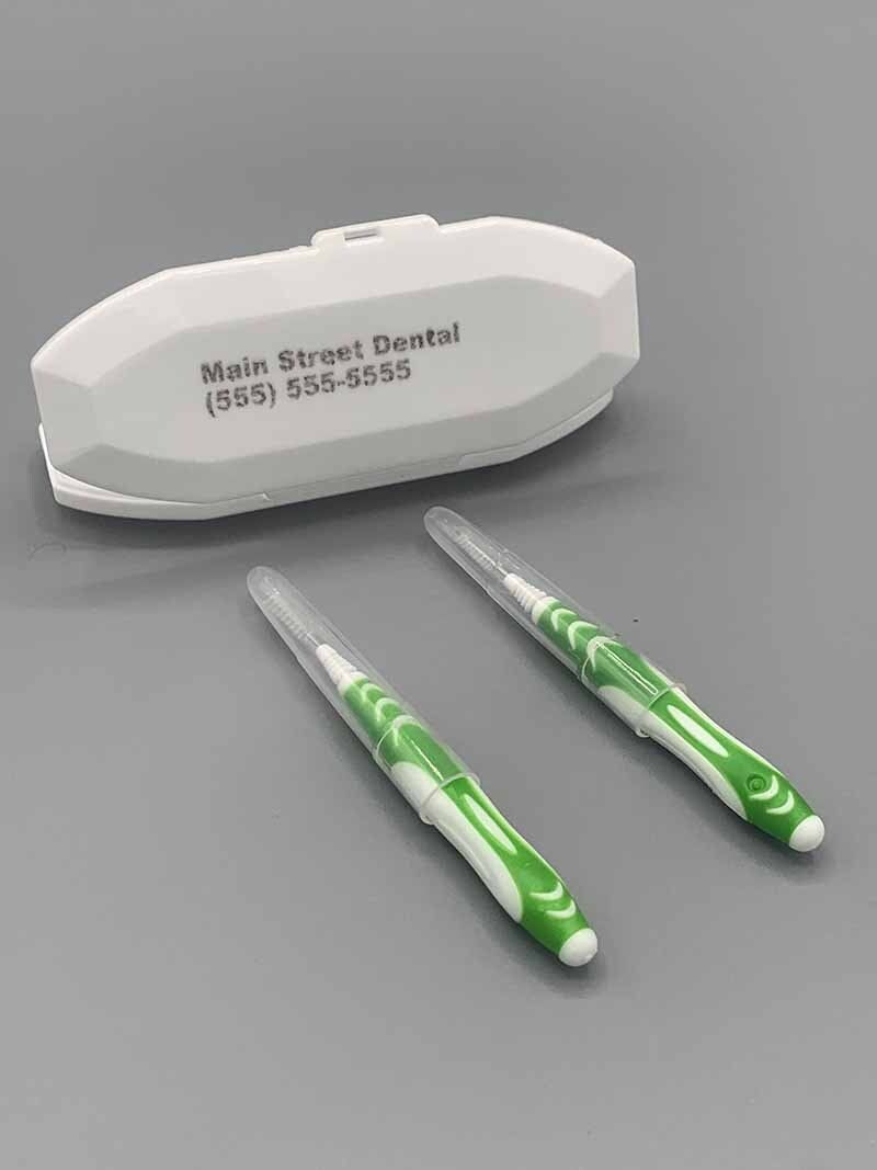 Two green and white interdental brushes are sitting next to a white case.