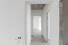 Unfinished white hallway with doorways, exposed wiring, and concrete floor.