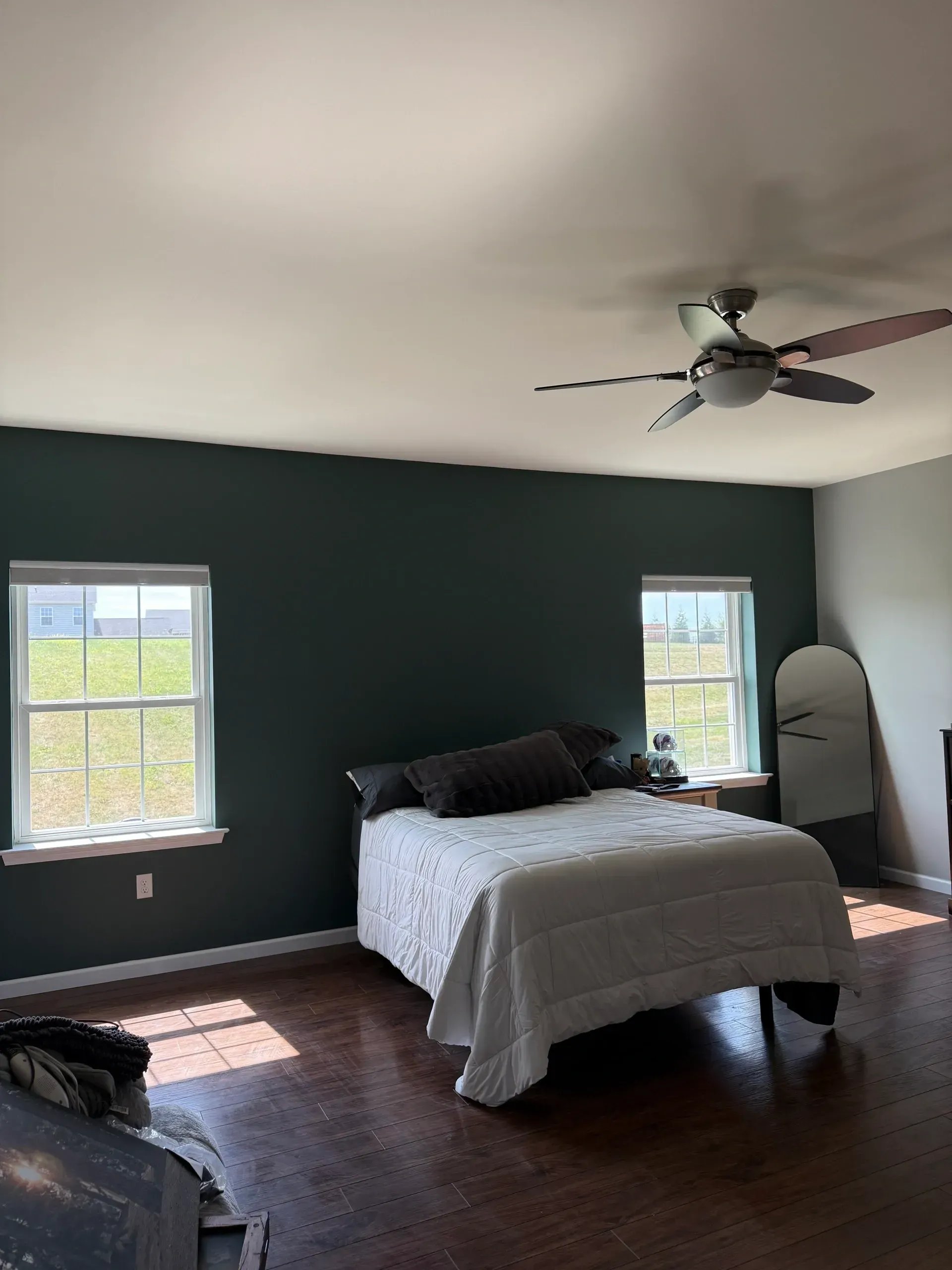 Bedroom with dark green walls, white bedding, two windows, and a ceiling fan.