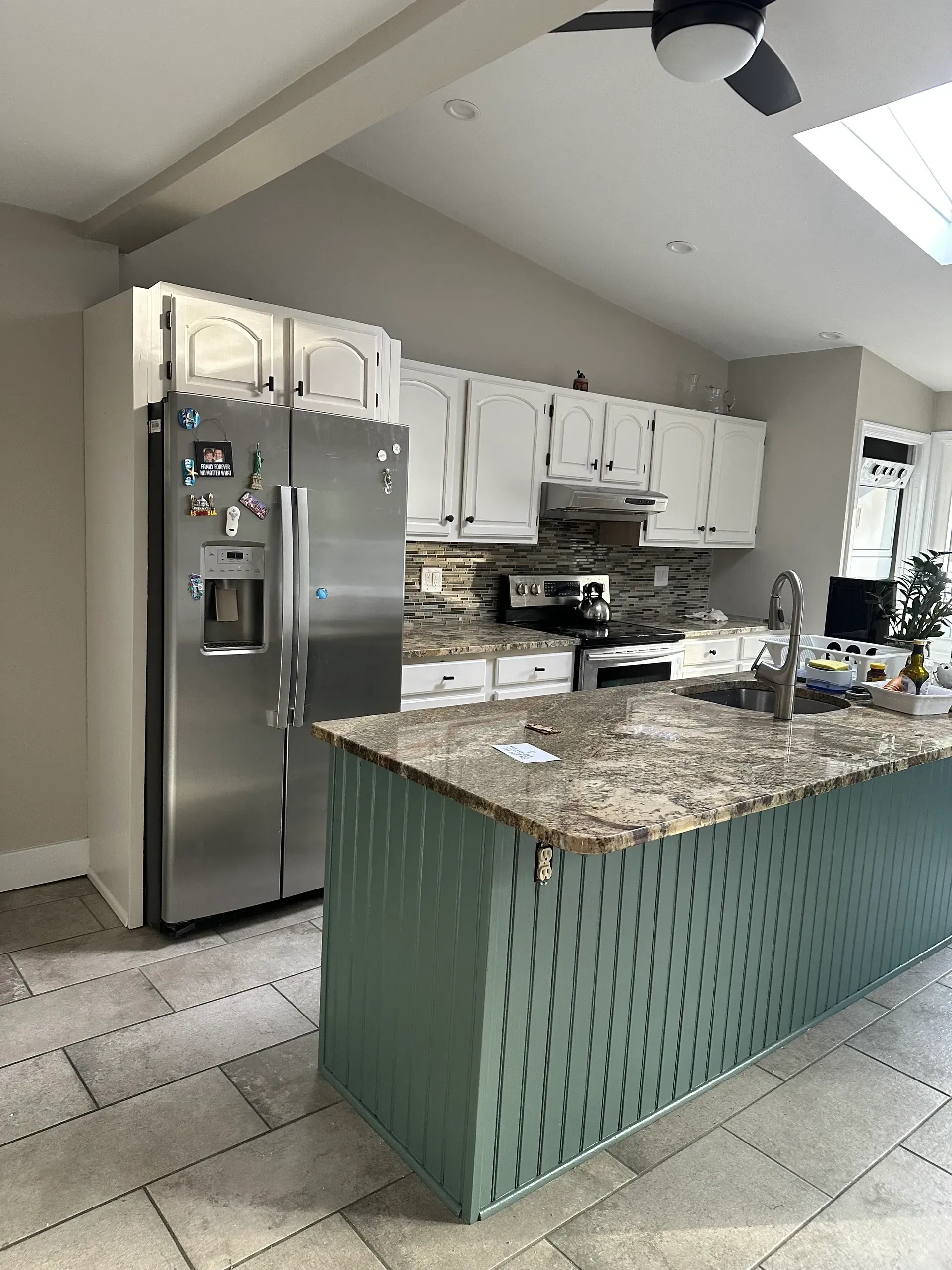 Modern kitchen with stainless fridge, white cabinets, and a large granite island with green base cabinets