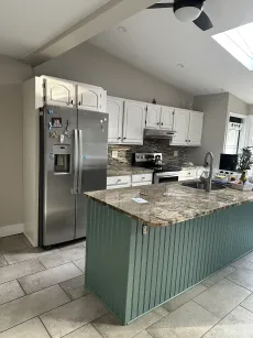 Modern kitchen with stainless fridge, white cabinets, and a large granite island with green base cabinets