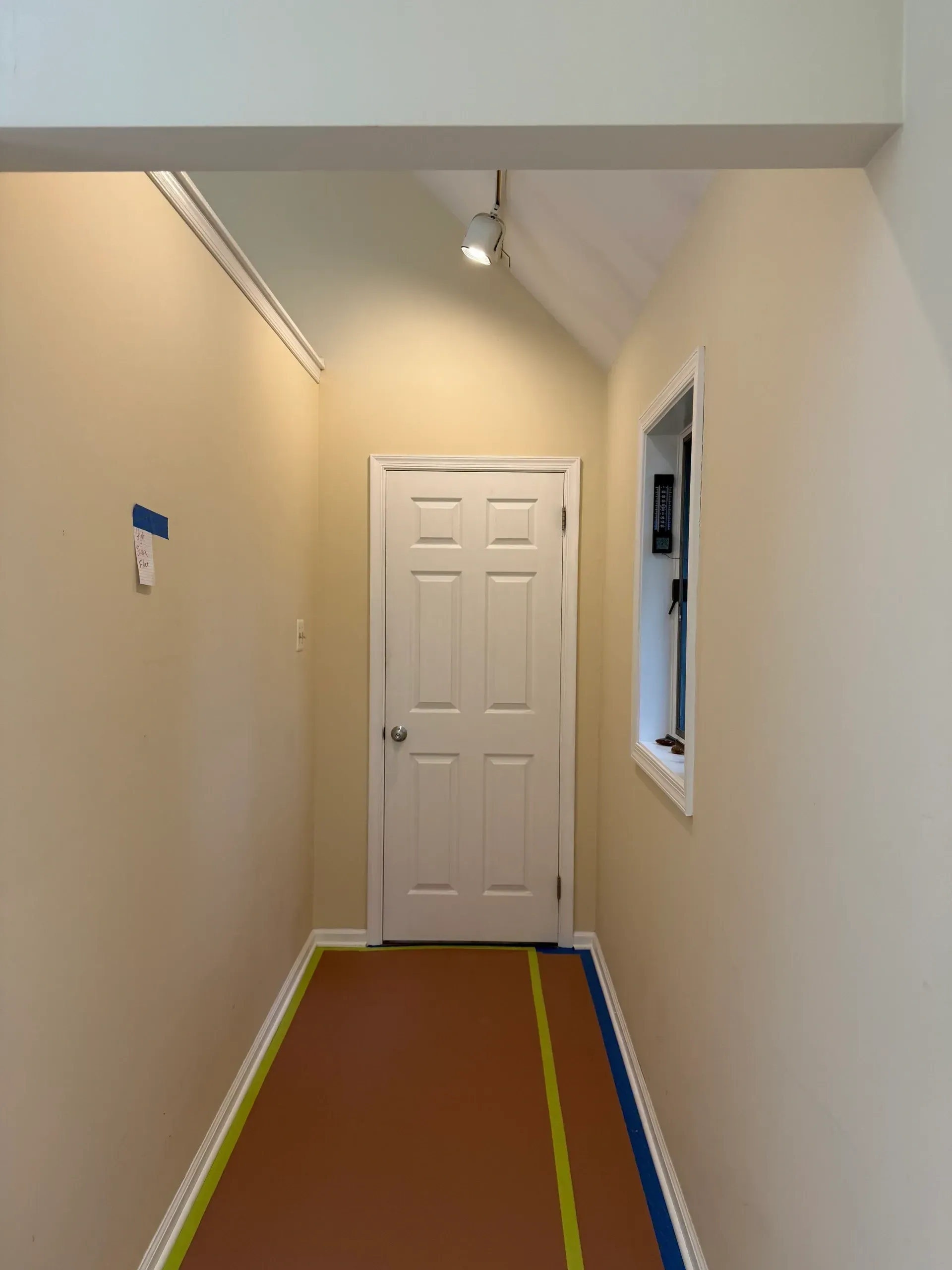 Narrow hallway with white door at the end, beige walls, and colorful tape lines on the floor