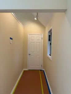 Narrow hallway with white door at the end, beige walls, and colorful tape lines on the floor