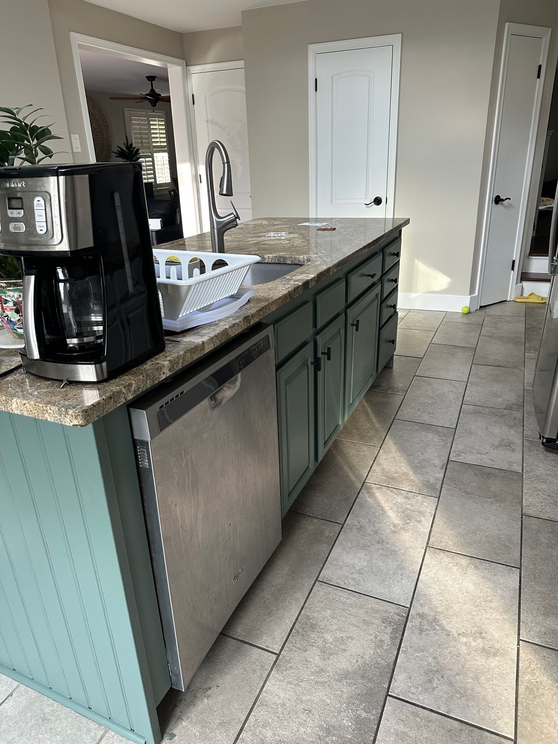 Kitchen with granite island, coffee maker, stainless dishwasher, and tiled floor, viewed from the side.