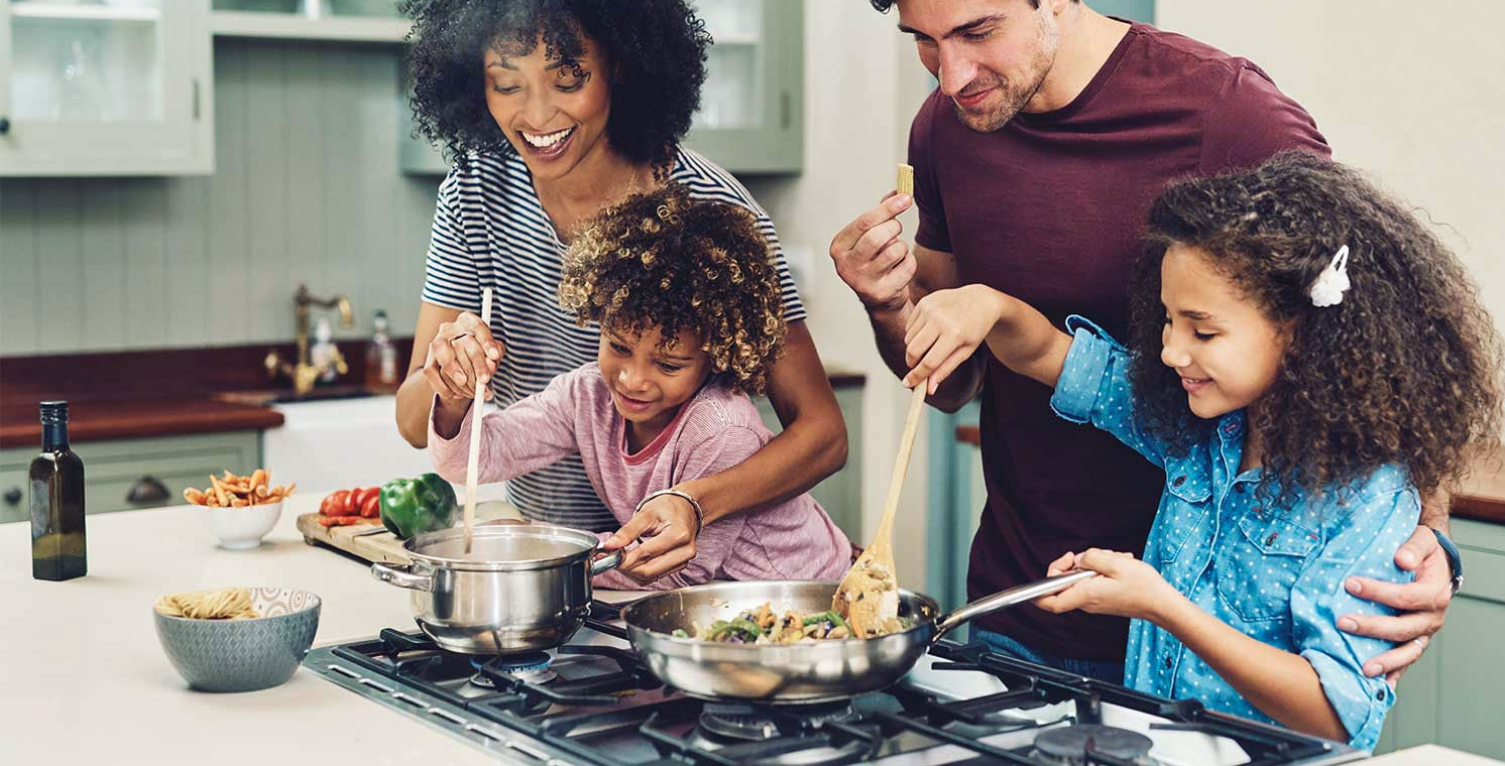 Family cooking together in a bright kitchen, smiling while stirring food on a stovetop.