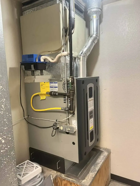 Industrial HVAC furnace with metal ductwork and yellow gas line in a utility closet