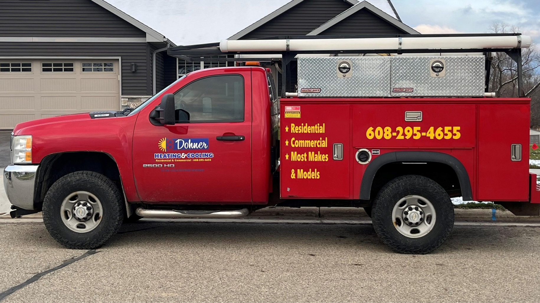 Red utility truck with ladder rack and company decals parked in front of a house.