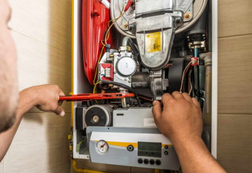 Technician repairing a wall-mounted boiler with tools and exposed internal components