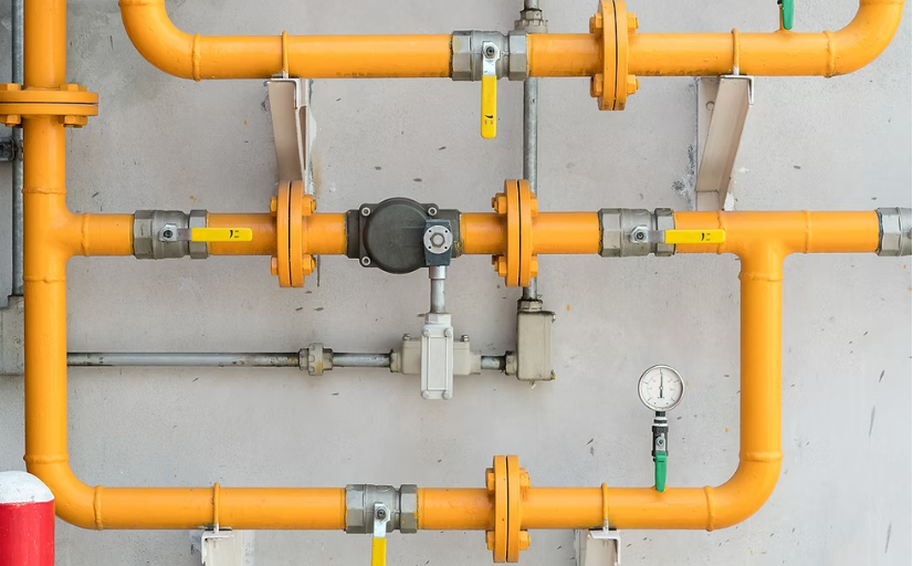 Orange industrial pipes with valves and gauges on a gray wall