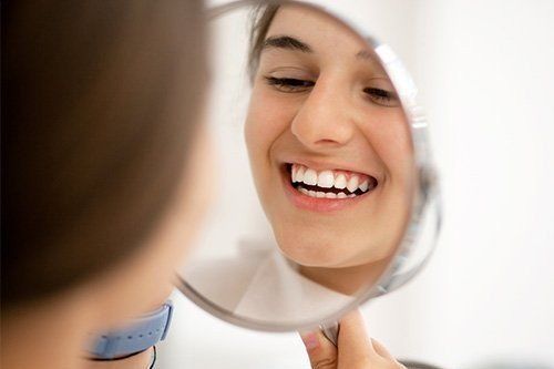 a woman is smiling while looking at her teeth in a mirror .