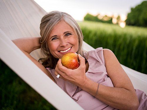 A woman is laying in a hammock holding an apple.