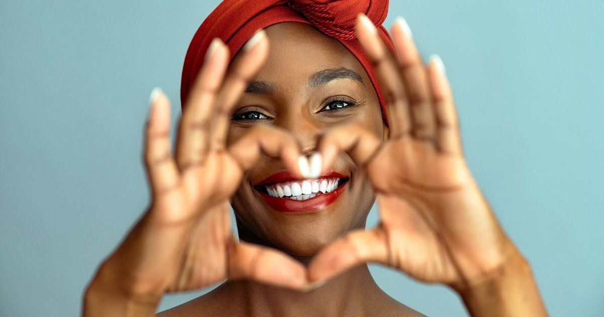 A woman is smiling and making a heart shape with her hands.