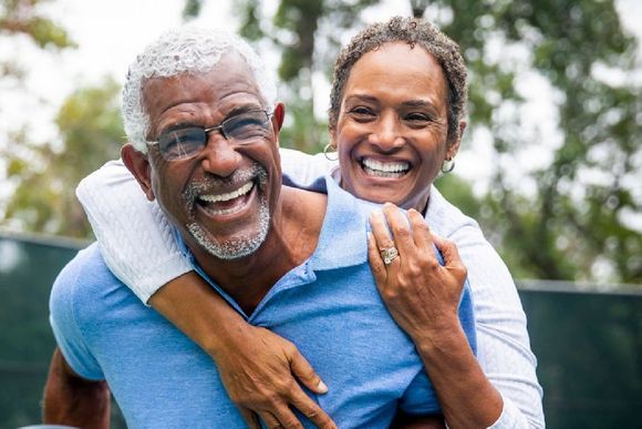 a man is giving a woman a piggyback ride and they are smiling .