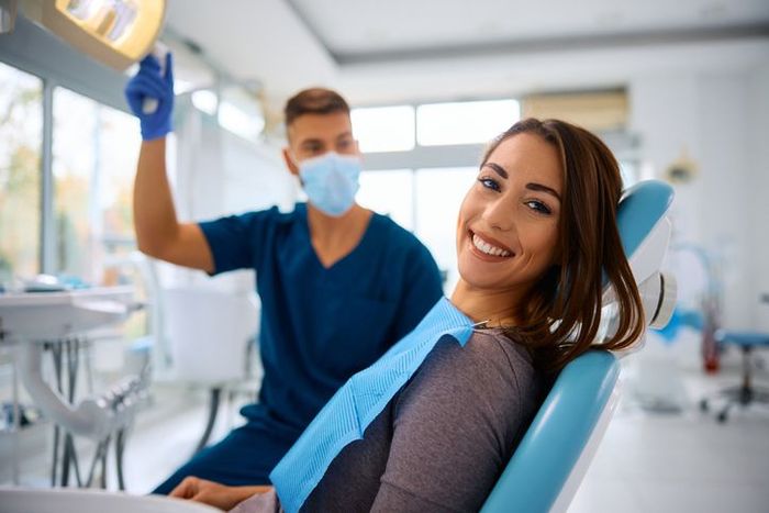 A woman is sitting in a dental chair with a dentist in the background.