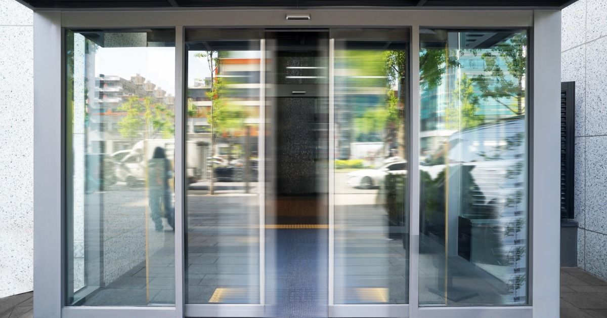An automatic sliding glass entrance with motion blur, reflections, and cars visible outside a modern
