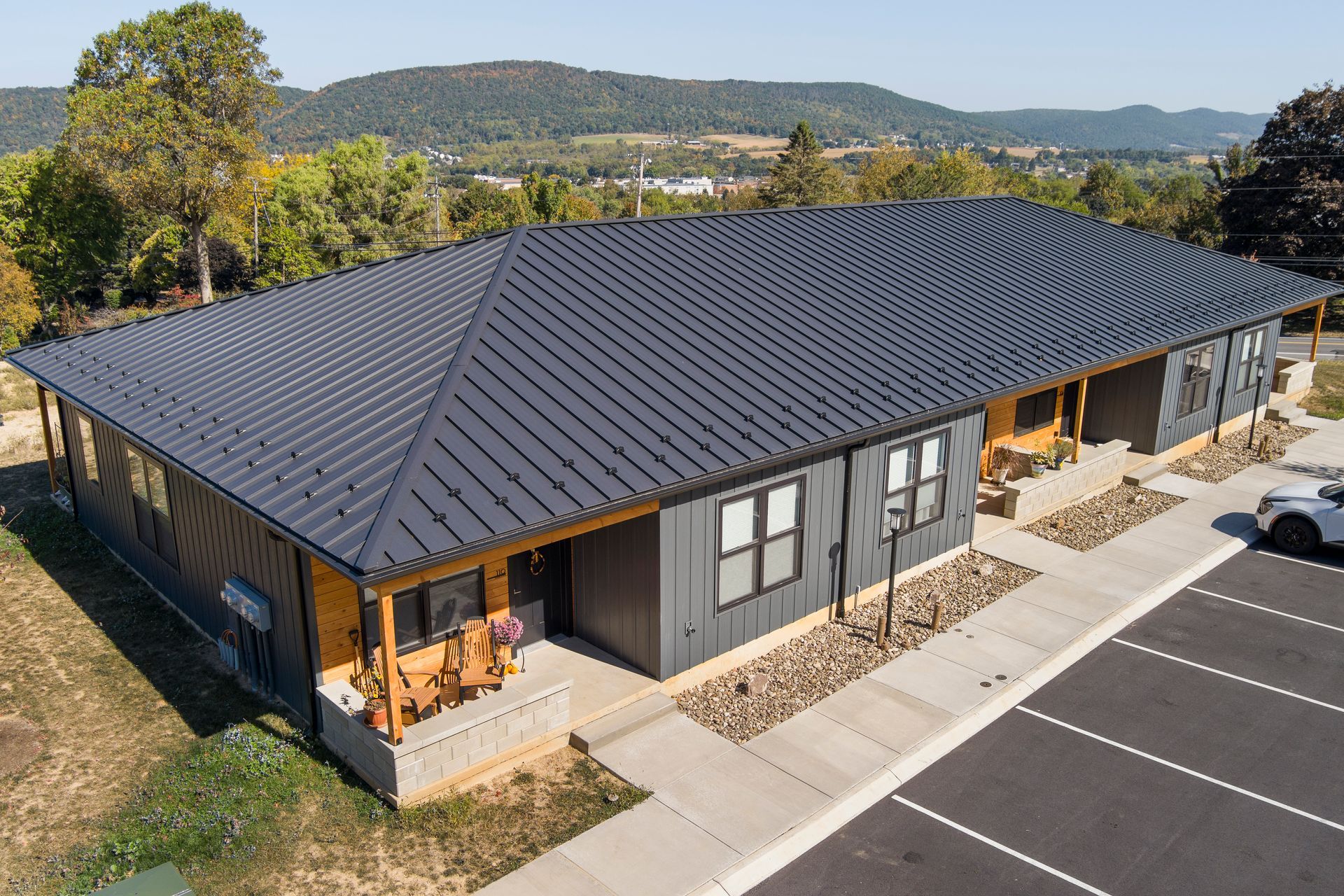 An aerial view of a single-story commercial building with a black metal roof, gray siding, and a parking lot.
