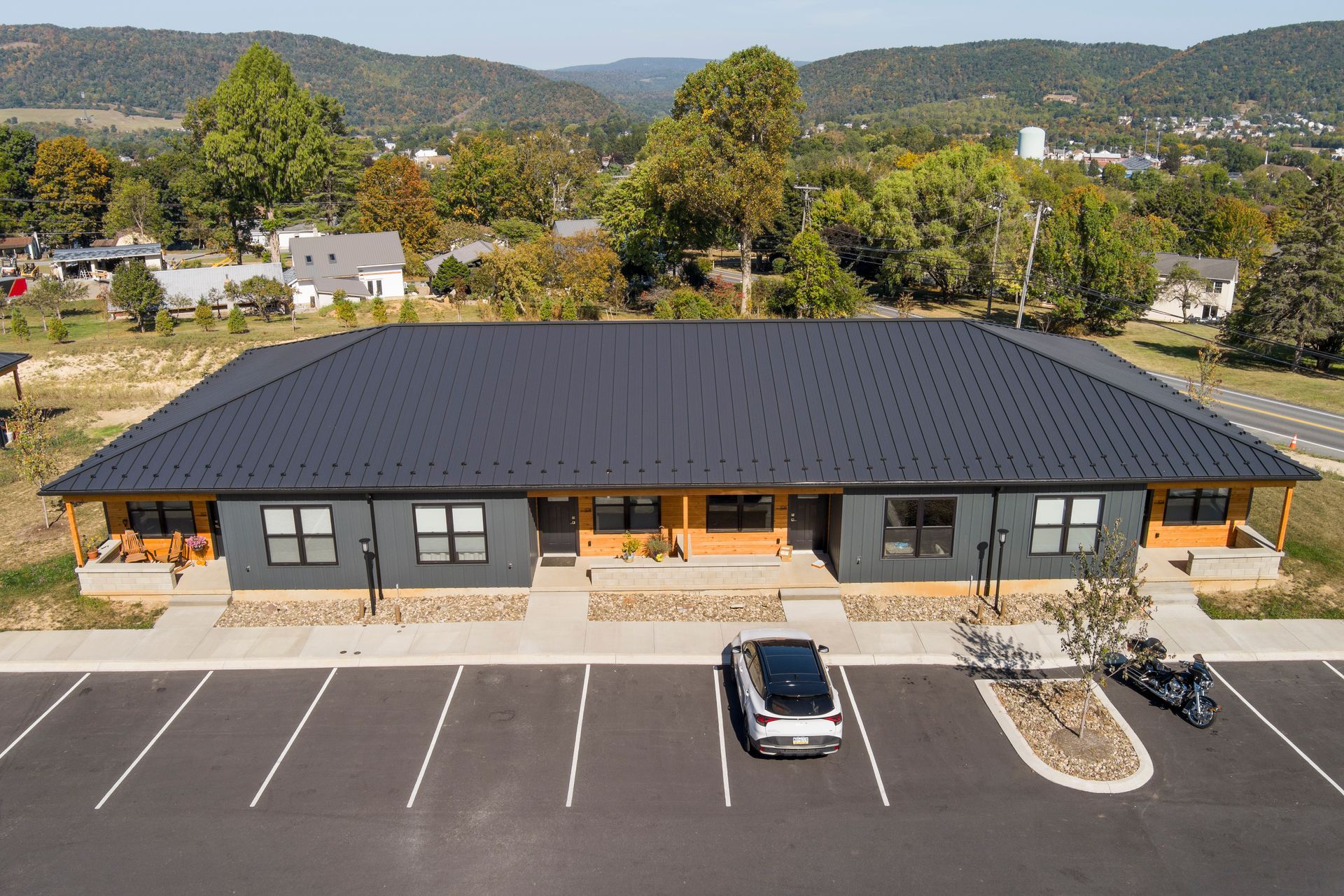 An aerial view of a single-story gray building with a dark metal roof, featuring a parking lot in the foreground.